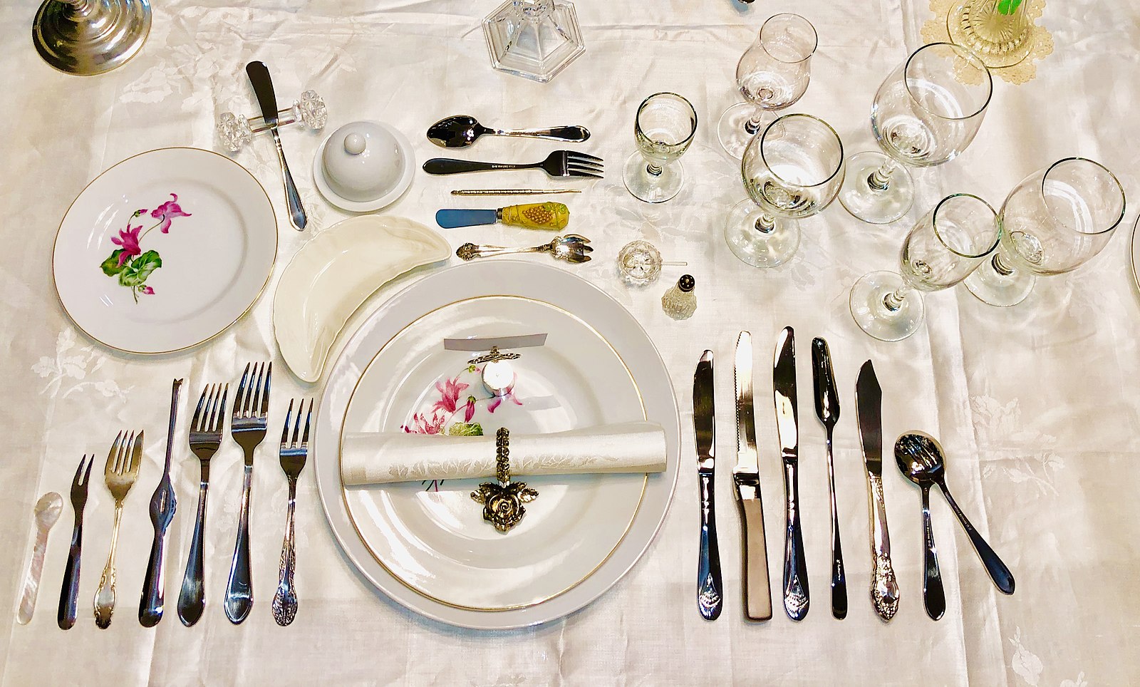 A place setting at a dining table, with many similar-looking utensils.