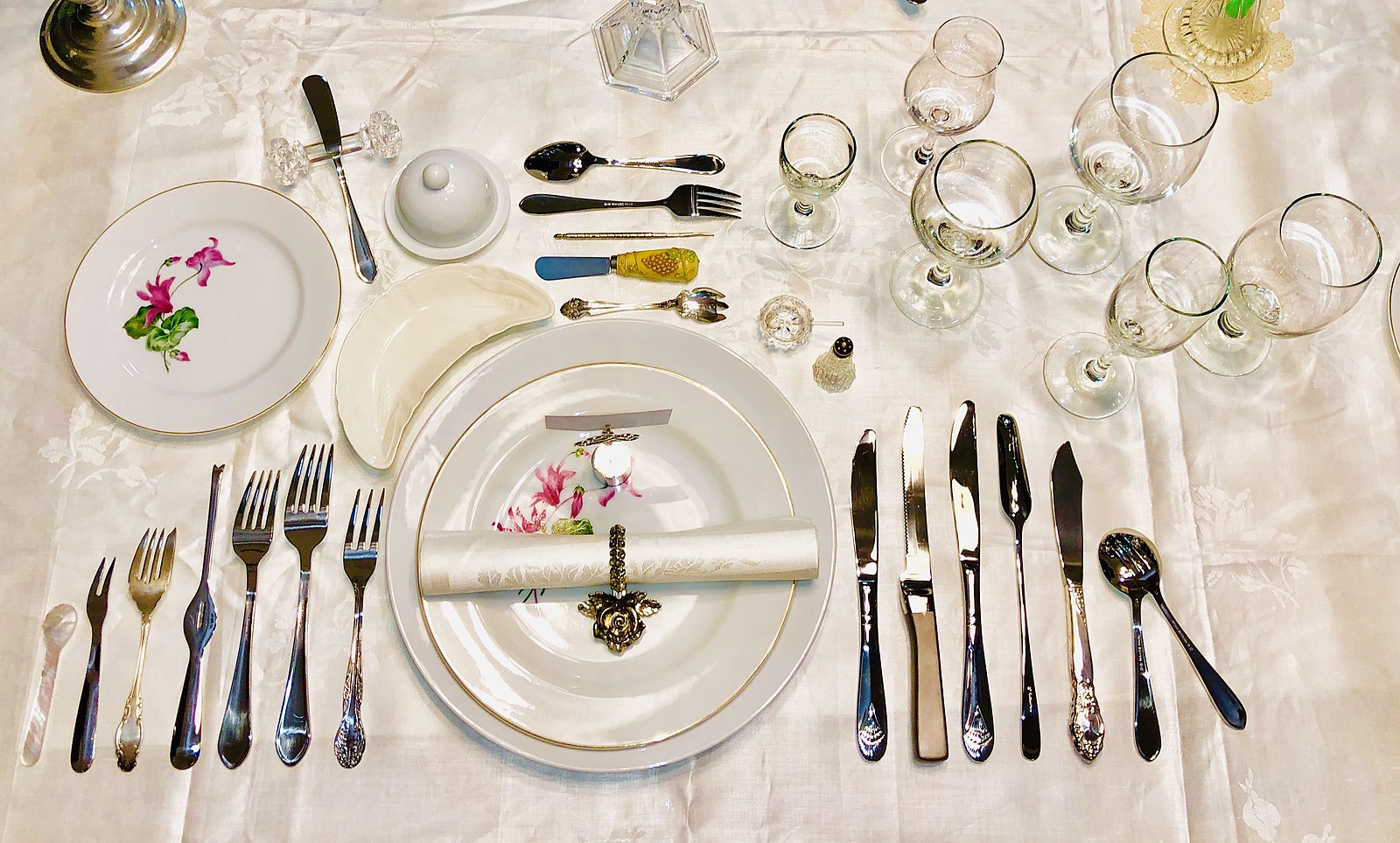 A place setting at a dining table, with many similar-looking utensils.
